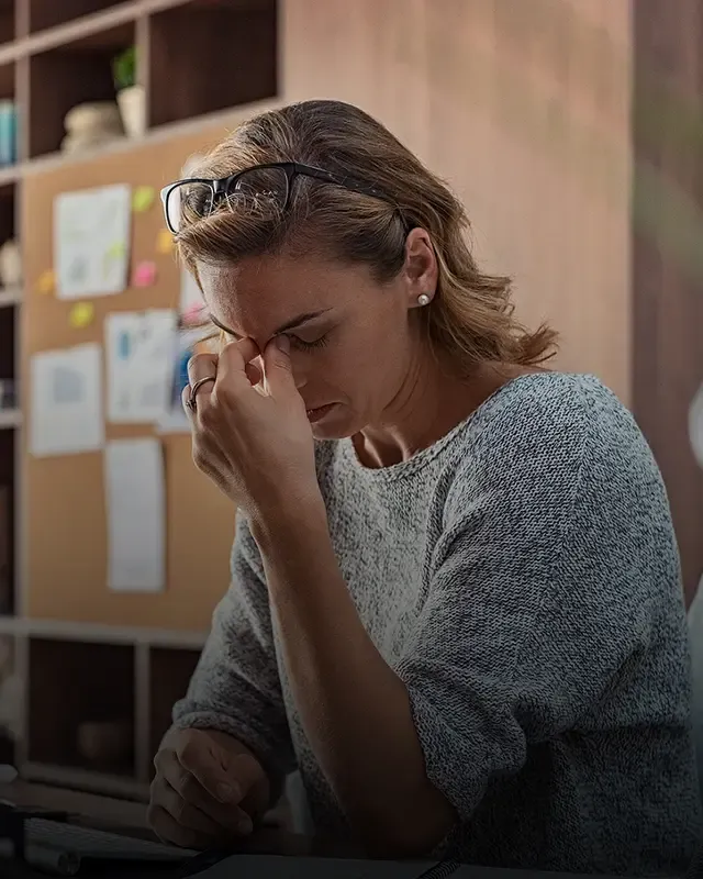 A woman pinching the bridge of her nose, trying to alleviate a headache