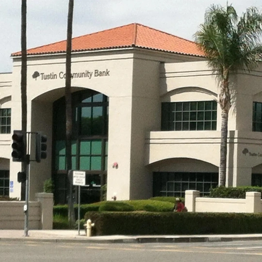 Large arched entrance, green-tinted windows, and a red-tiled roof. Palm trees and street signs are visible in the foreground along with a traffic light and sidewalk