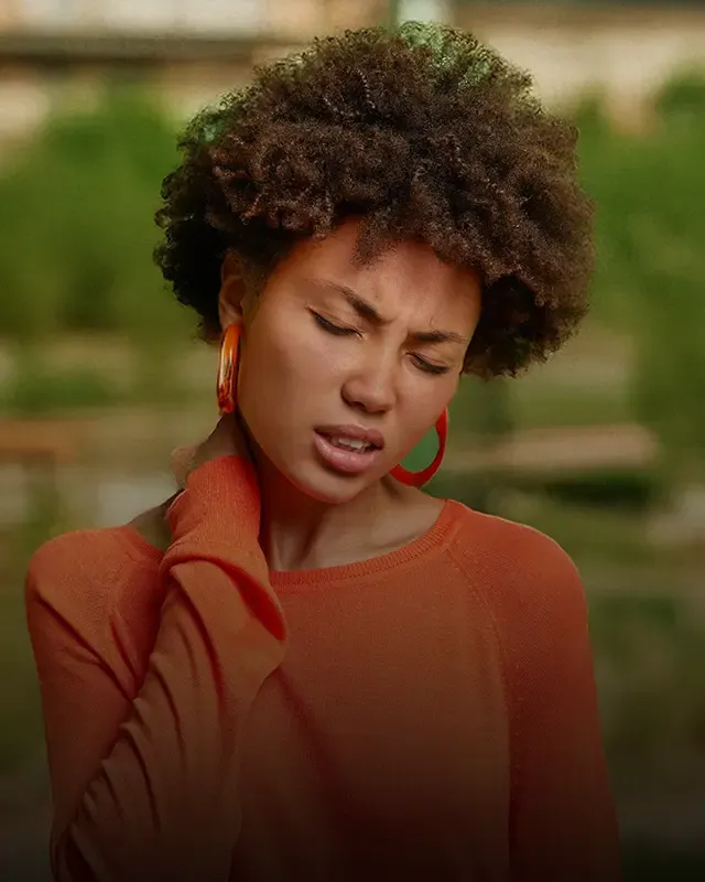A woman massaging the back of her neck, face grimacing in pain