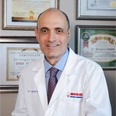 A medium close up photo of Dr. Gregory Salemn smiling in front of his degrees and certificates at Salem Chiropractic